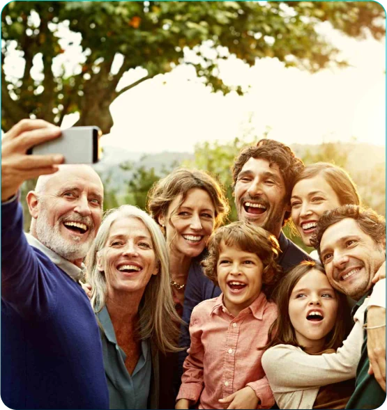 Família de várias gerações sorrindo juntas em uma selfie ao ar livre